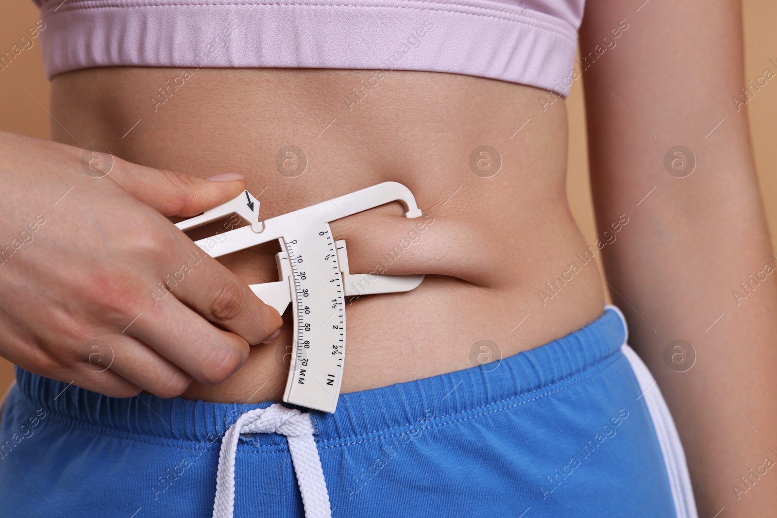 Photo of Woman measuring body fat with caliper on beige background, closeup