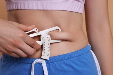 Photo of Woman measuring body fat with caliper on beige background, closeup