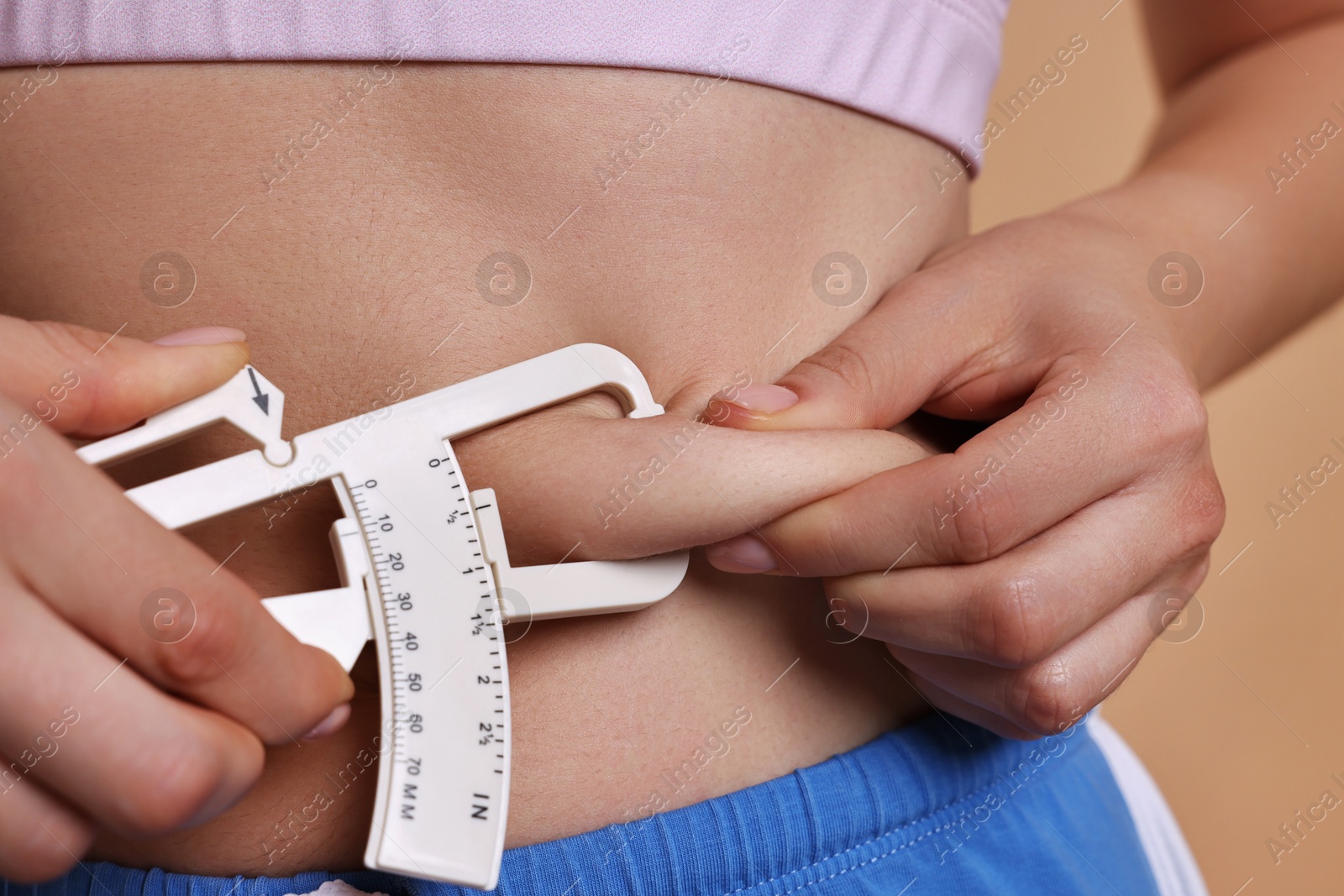 Photo of Woman measuring body fat with caliper on beige background, closeup