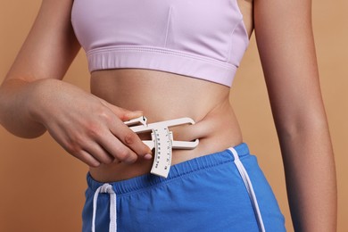 Photo of Woman measuring body fat with caliper on beige background, closeup