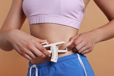 Photo of Woman measuring body fat with caliper on beige background, closeup