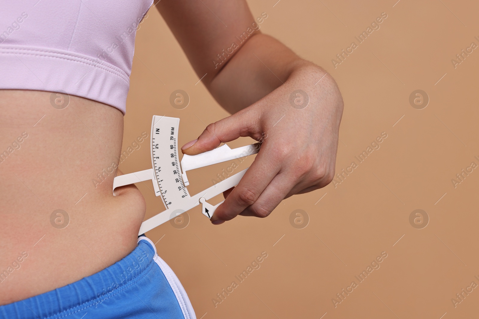 Photo of Woman measuring body fat with caliper on beige background, closeup