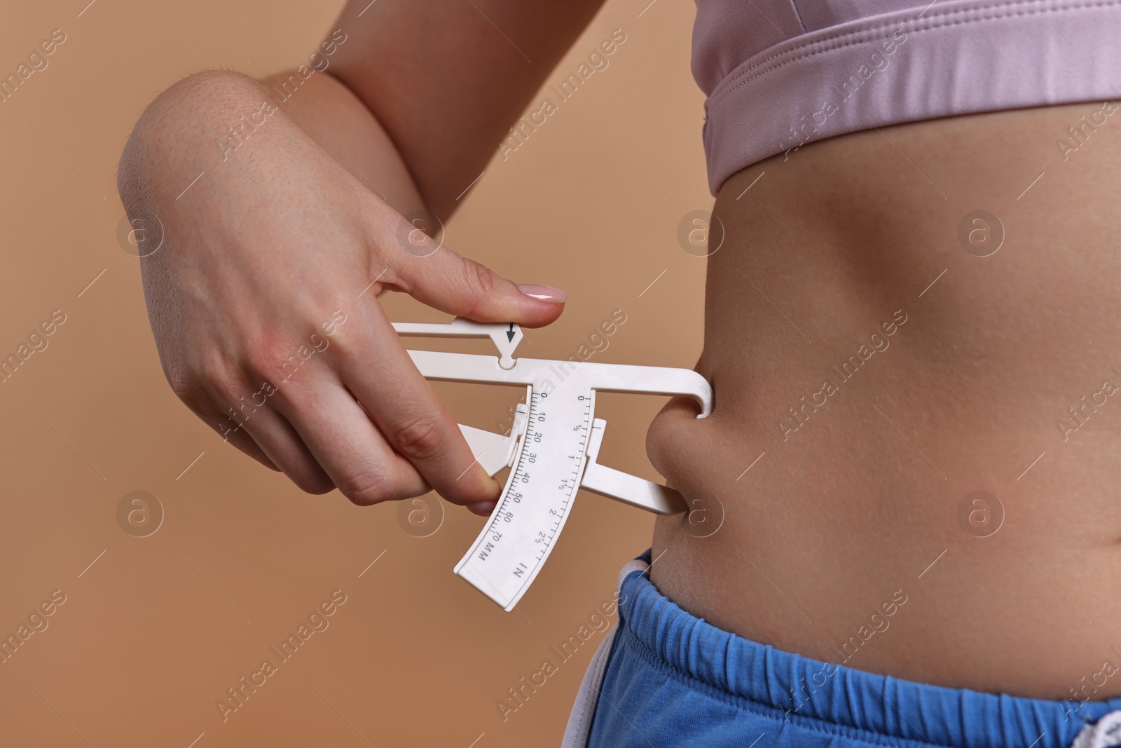 Photo of Woman measuring body fat with caliper on beige background, closeup