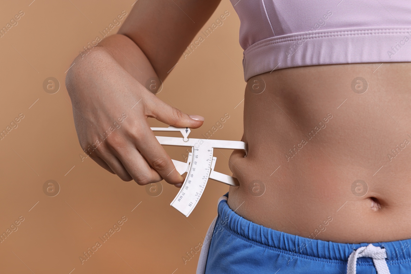 Photo of Woman measuring body fat with caliper on beige background, closeup