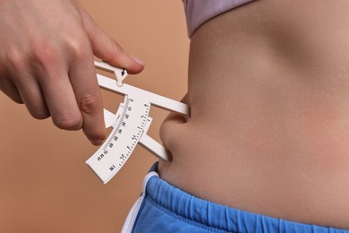 Photo of Woman measuring body fat with caliper on beige background, closeup