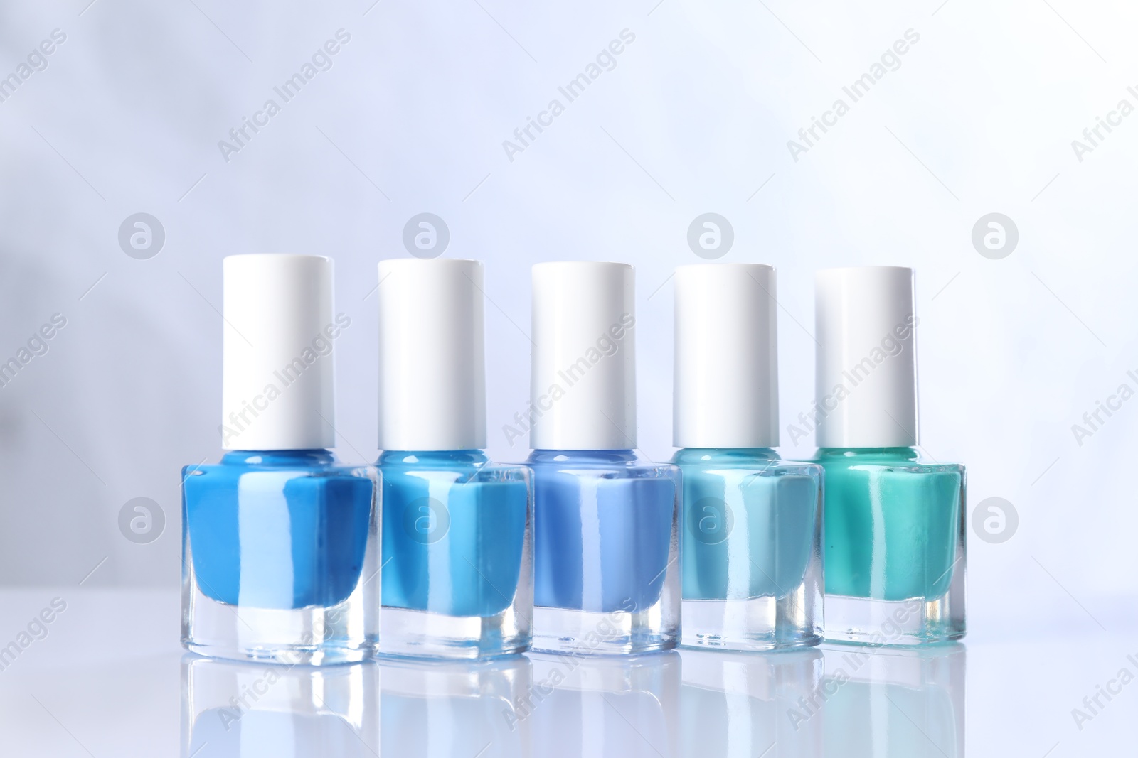 Photo of Set of nail polishes in bottles on mirror table against white background