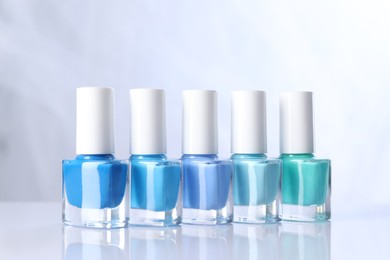 Photo of Set of nail polishes in bottles on mirror table against white background