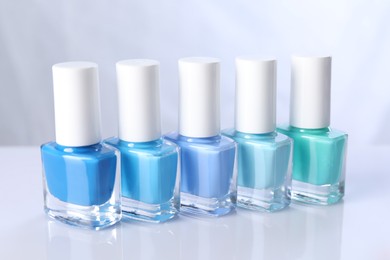 Photo of Set of nail polishes in bottles on mirror table against white background, closeup