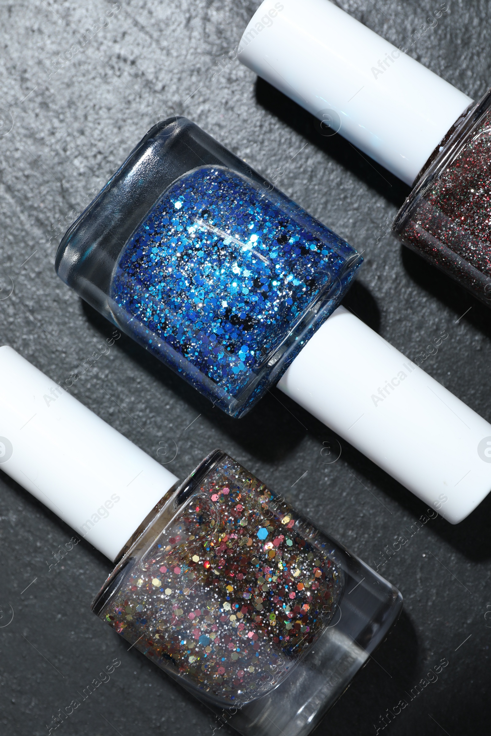 Photo of Set of different nail polishes in bottles on dark textured table, flat lay