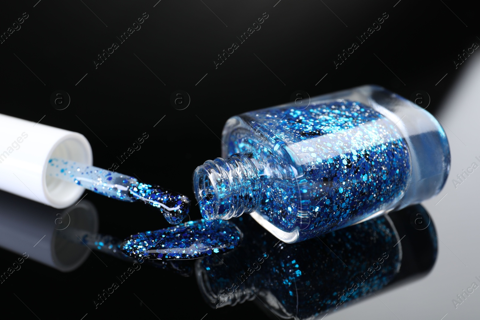 Photo of Open nail polish in bottle and brush on black mirror surface, closeup