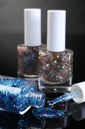 Photo of Glitter nail polishes in bottles and brush on black mirror surface, closeup