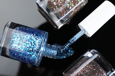 Photo of Glitter nail polishes in bottles and brush on mirror surface, flat lay