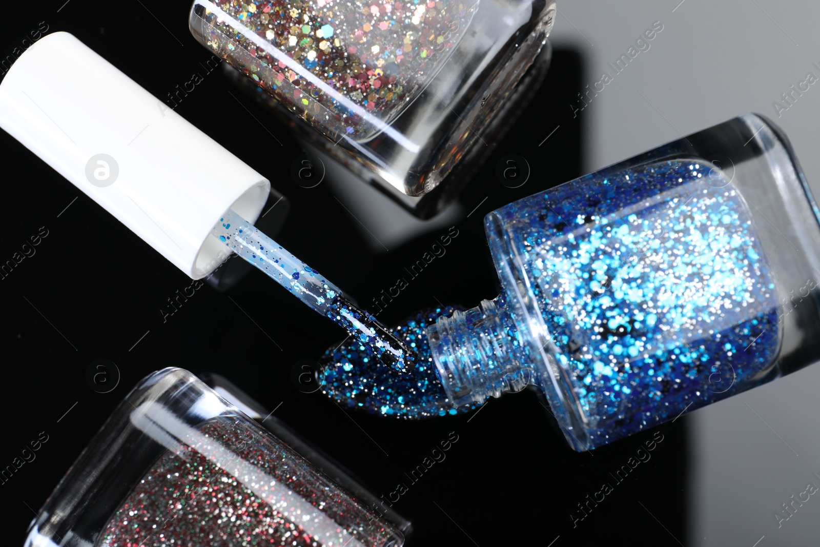 Photo of Glitter nail polishes in bottles and brush on mirror surface, flat lay