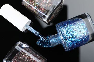 Photo of Glitter nail polishes in bottles and brush on mirror surface, flat lay