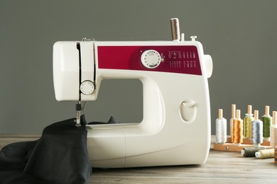 Sewing machine, black fabric and craft accessories on wooden table against gray background