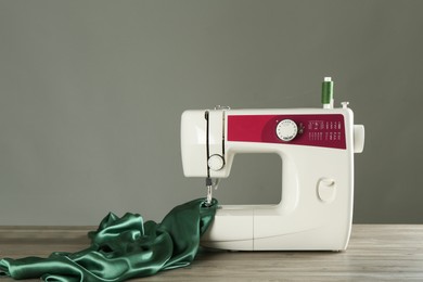 Photo of Sewing machine with green fabric on wooden table against gray background