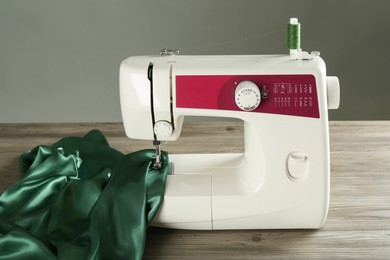 Photo of Sewing machine with green fabric on wooden table against gray background