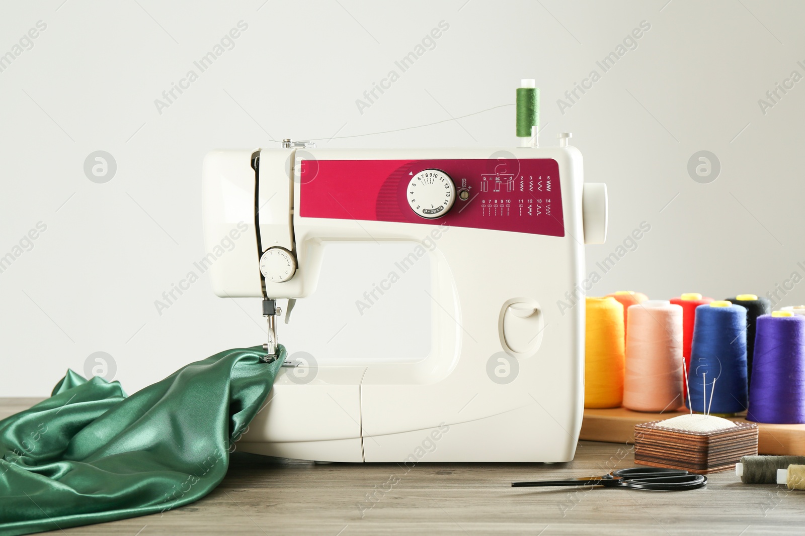 Photo of Sewing machine, green fabric and craft accessories on wooden table against light background