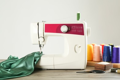 Sewing machine, green fabric and craft accessories on wooden table against light background