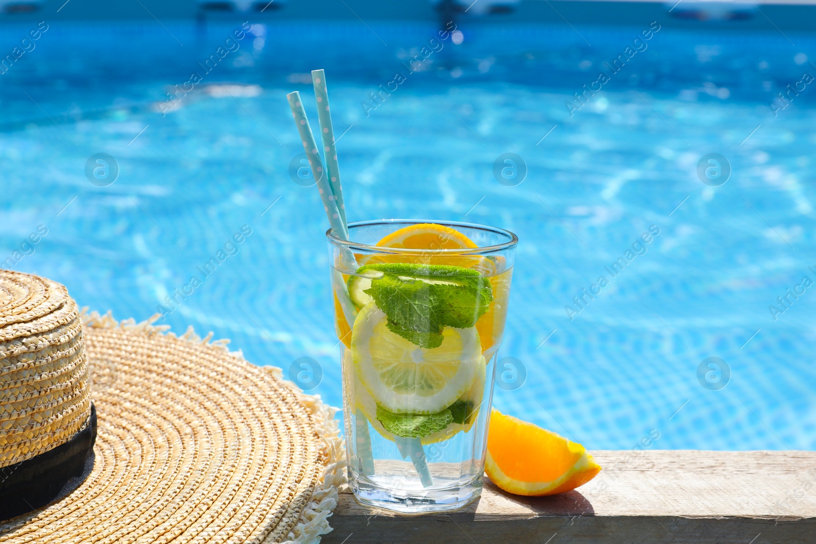 Photo of Tasty cocktail in glass and straw hat near swimming pool outdoors