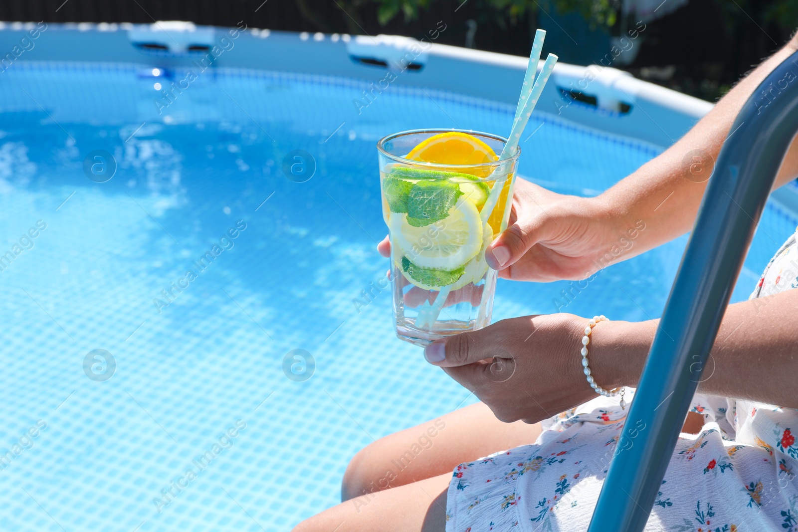 Photo of Woman holding tasty cocktail in glass near swimming pool outdoors, closeup