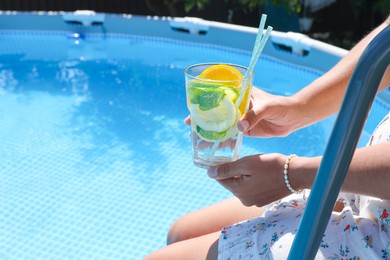 Photo of Woman holding tasty cocktail in glass near swimming pool outdoors, closeup