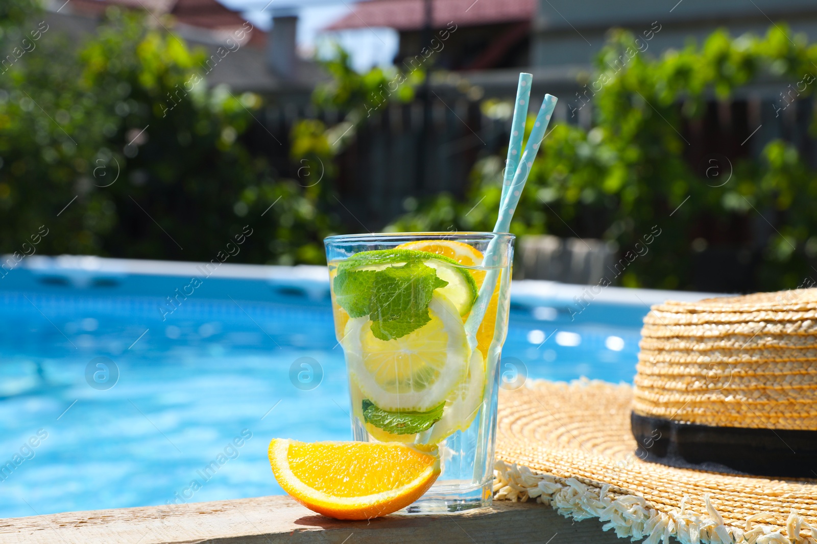 Photo of Tasty cocktail in glass and straw hat near swimming pool outdoors