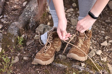 Woman tying shoelace of trekking shoes outdoors, closeup