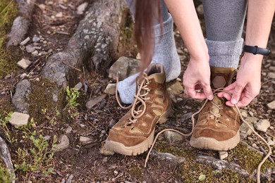 Photo of Woman tying shoelace of trekking shoes outdoors, closeup