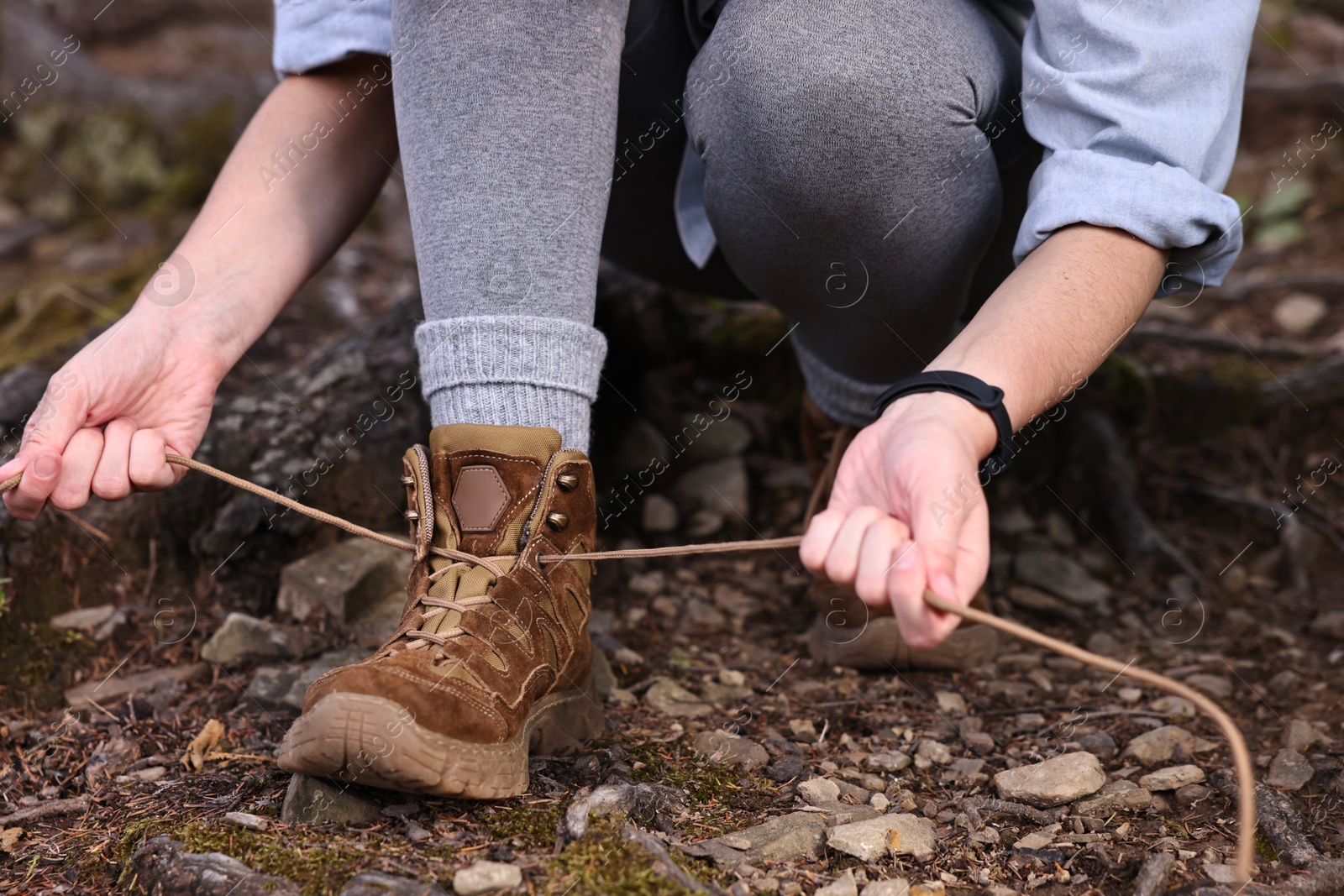 Photo of Woman tying shoelace of trekking shoes outdoors, closeup