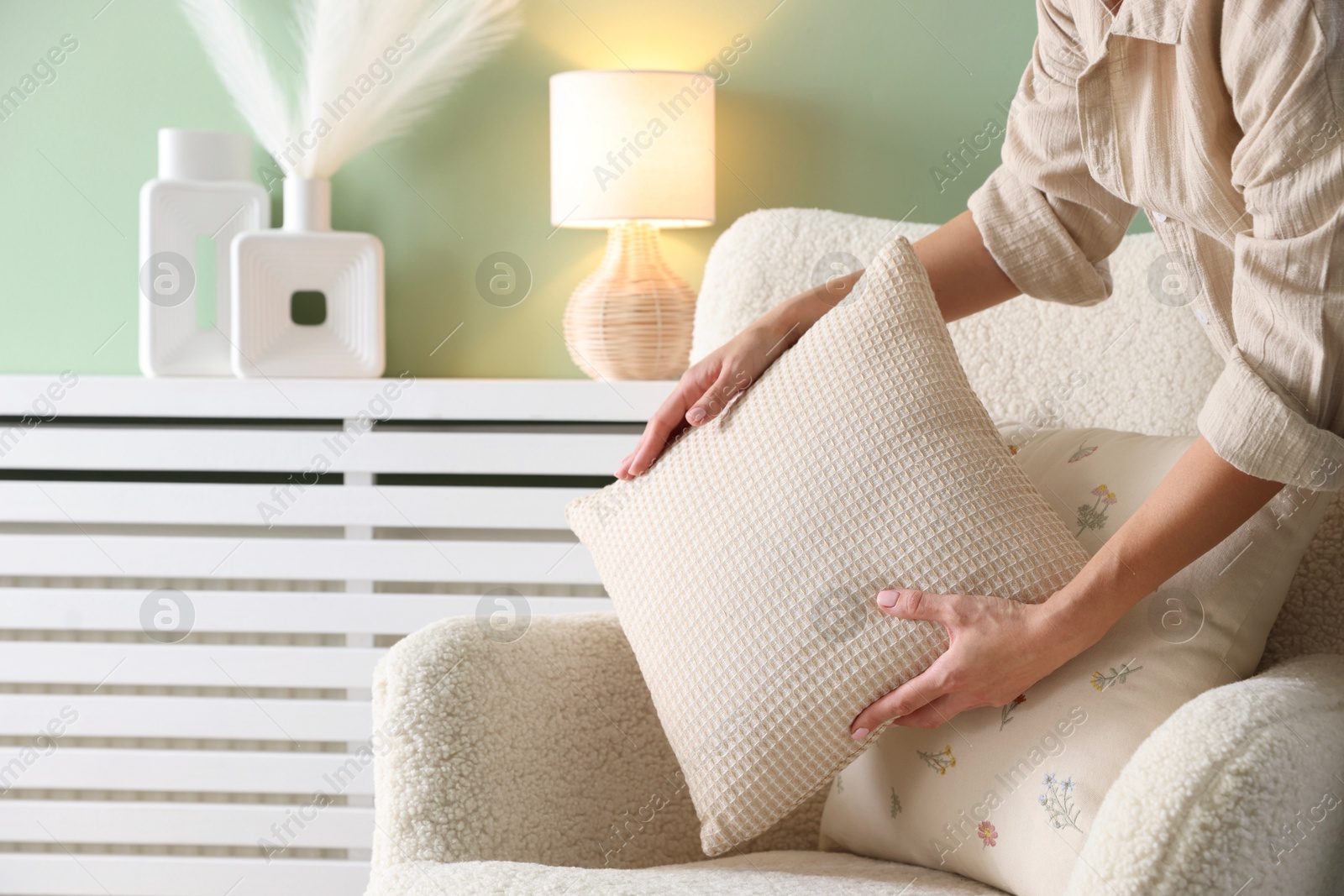 Photo of Woman putting soft pillow onto light armchair in living room, closeup