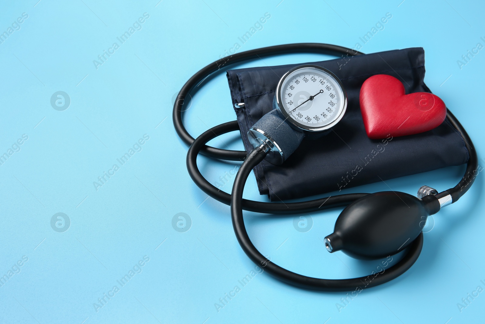 Photo of Blood pressure measuring device and heart figure on light blue background, space for text