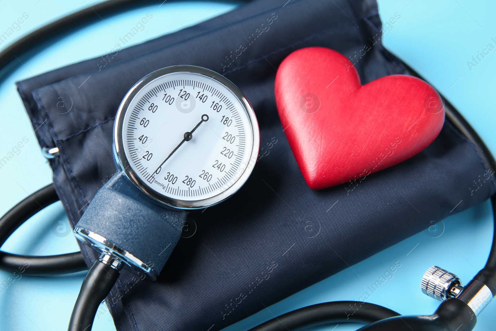 Photo of Blood pressure measuring device and heart figure on light blue background, closeup