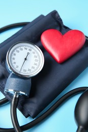 Photo of Blood pressure measuring device and heart figure on light blue background, closeup