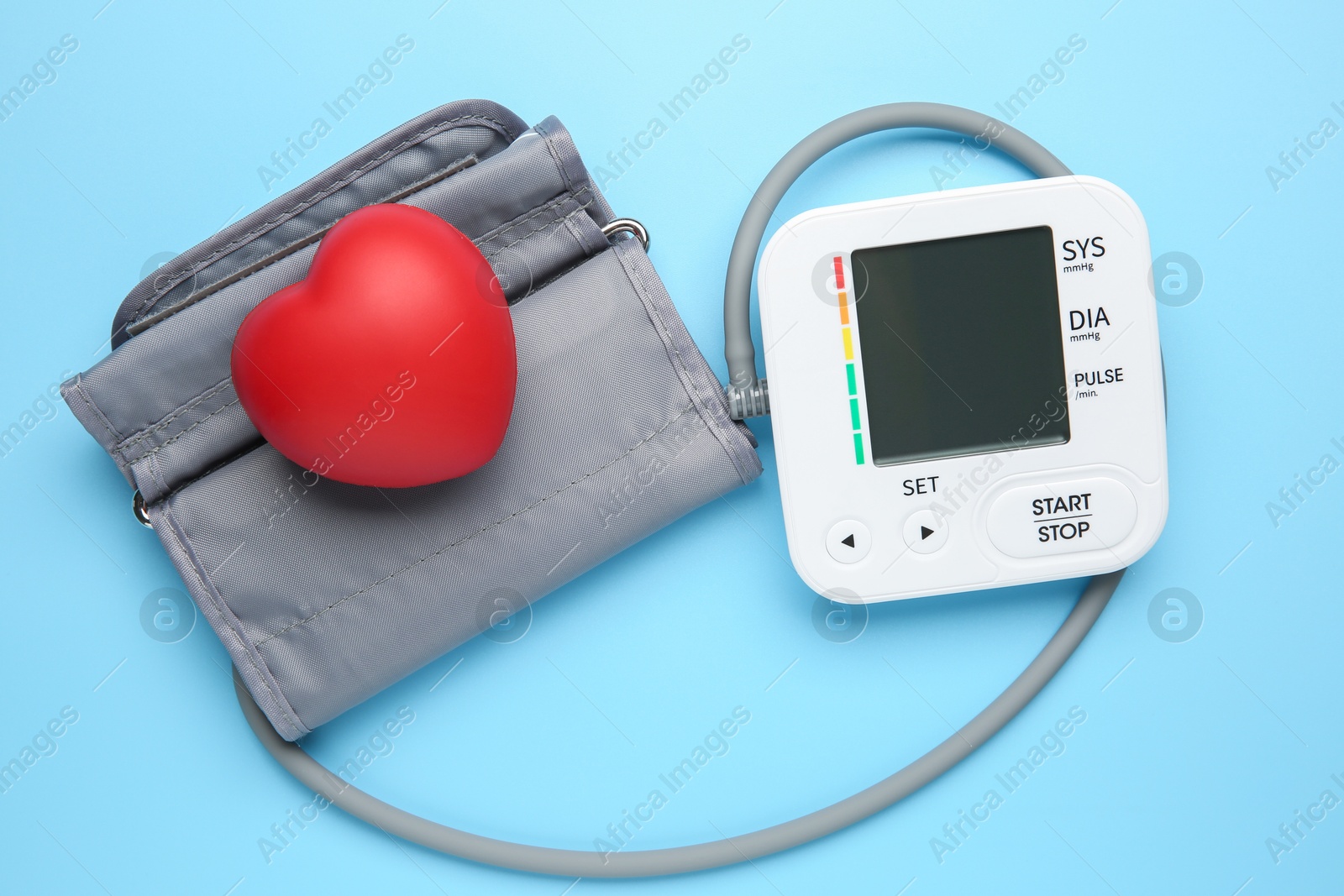 Photo of Blood pressure measuring device and squeeze heart on light blue background, top view