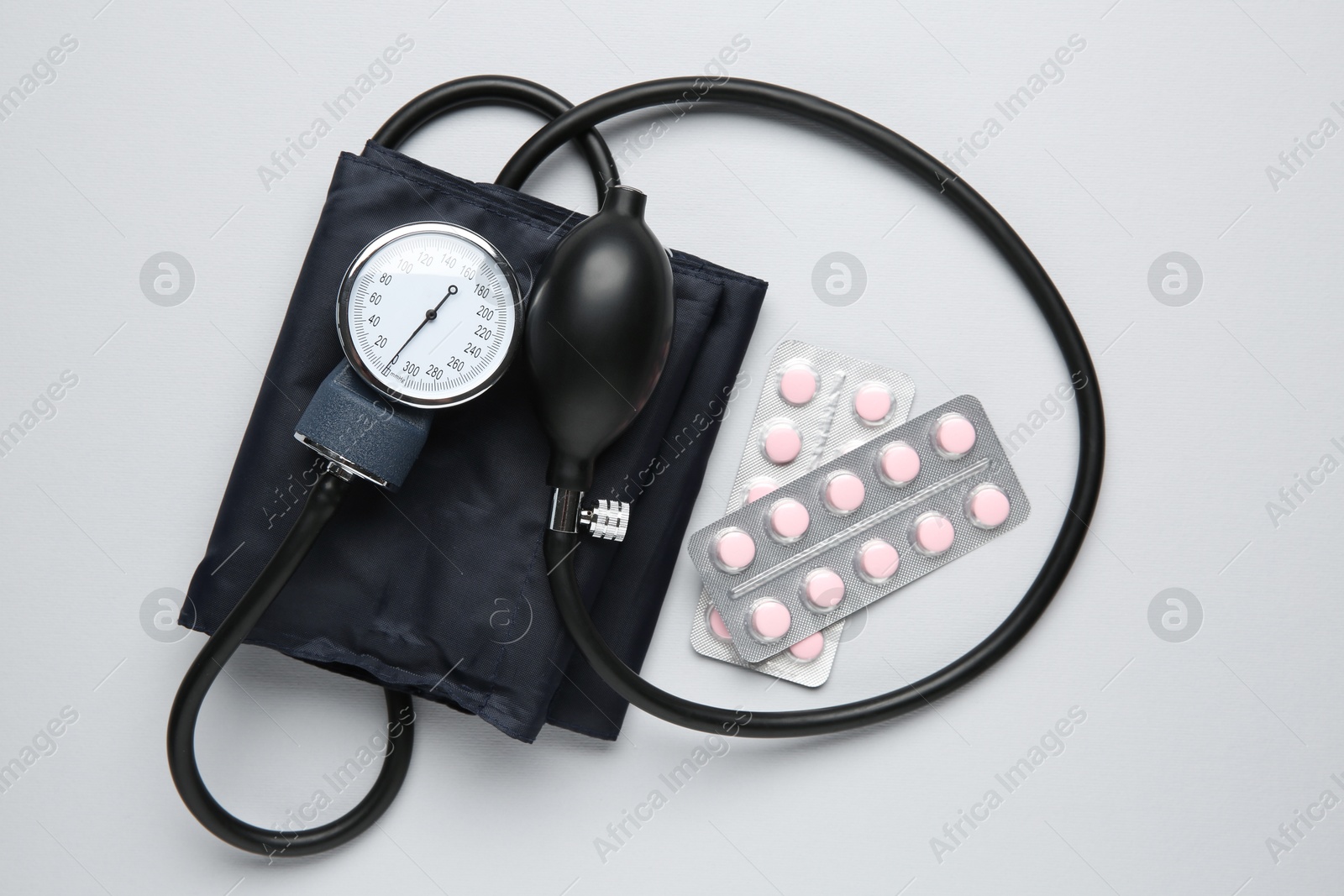 Photo of Blood pressure measuring device and pills on light grey background, top view