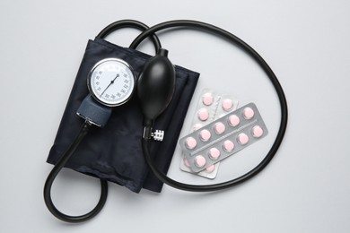 Blood pressure measuring device and pills on light grey background, top view