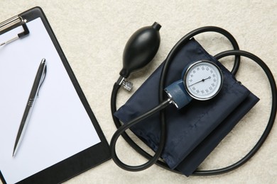 Photo of Blood pressure measuring device and clipboard on light textured background, top view