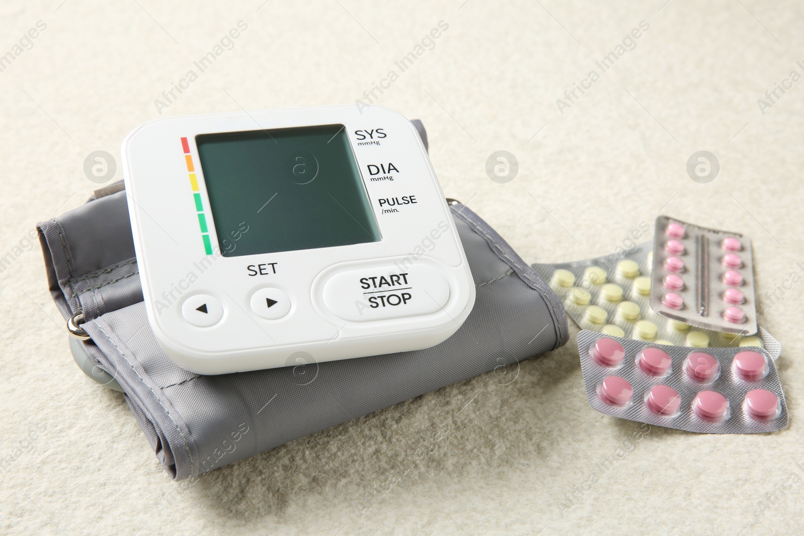 Photo of Blood pressure measuring device and pills on light textured background, closeup