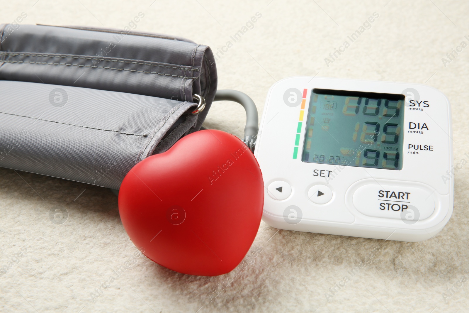 Photo of Blood pressure measuring device and squeeze heart on light textured background, closeup