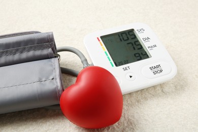 Photo of Blood pressure measuring device and squeeze heart on light textured background, closeup