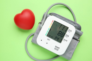 Photo of Blood pressure measuring device and squeeze heart on green background, top view