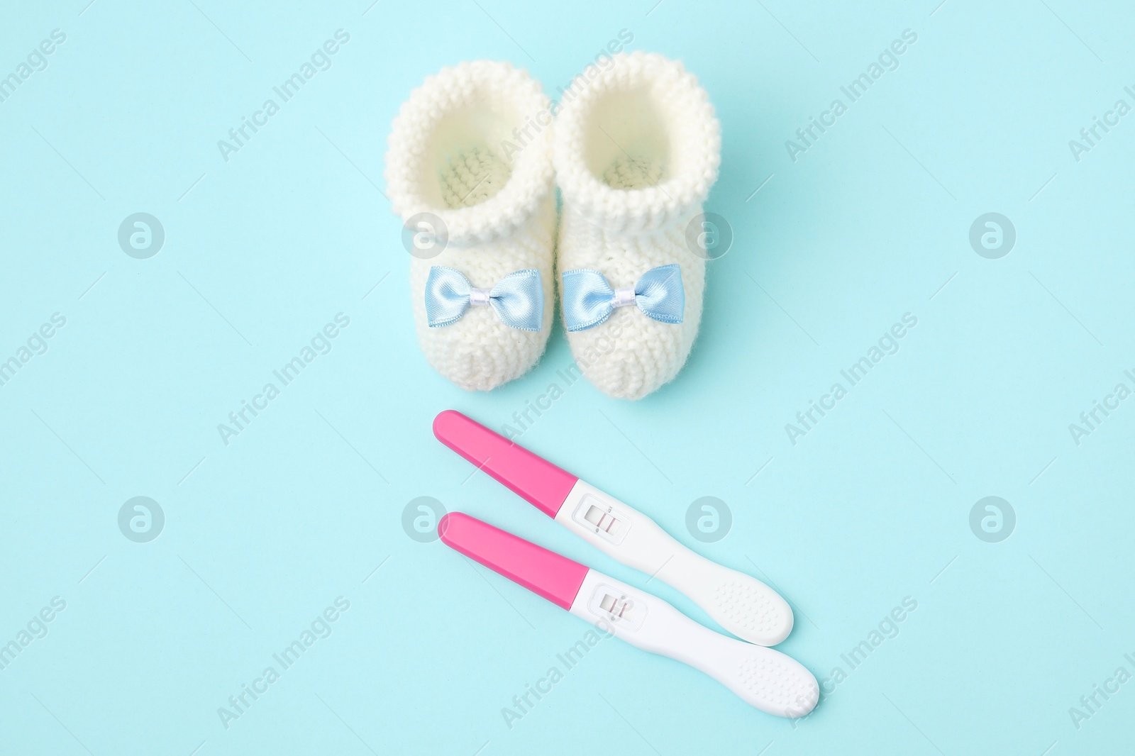 Photo of Pregnancy tests and knitted booties on light blue background, top view