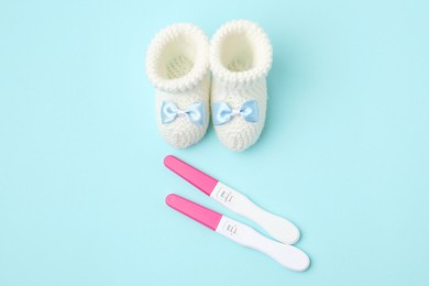 Photo of Pregnancy tests and knitted booties on light blue background, top view