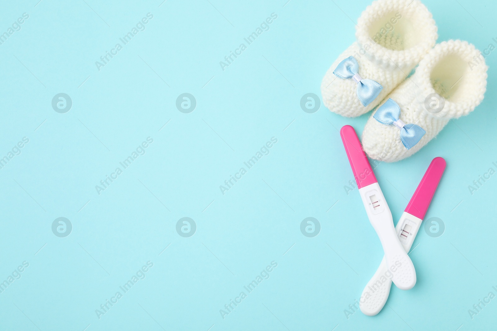 Photo of Pregnancy tests and knitted booties on light blue background, top view. Space for text