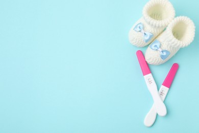 Photo of Pregnancy tests and knitted booties on light blue background, top view. Space for text