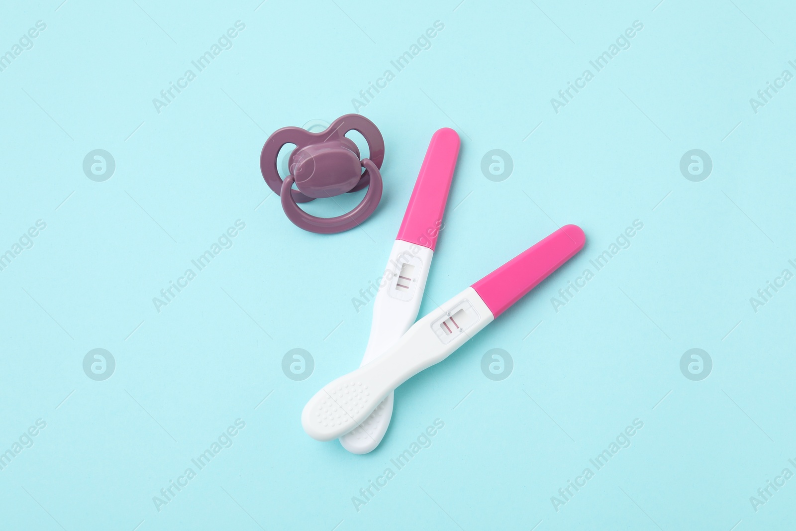 Photo of Pregnancy tests and pacifier on light blue background