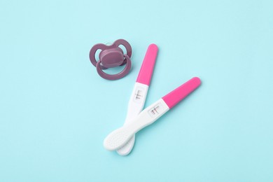 Photo of Pregnancy tests and pacifier on light blue background