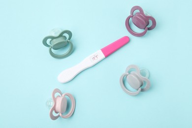 Photo of Pregnancy test and pacifiers on light blue background