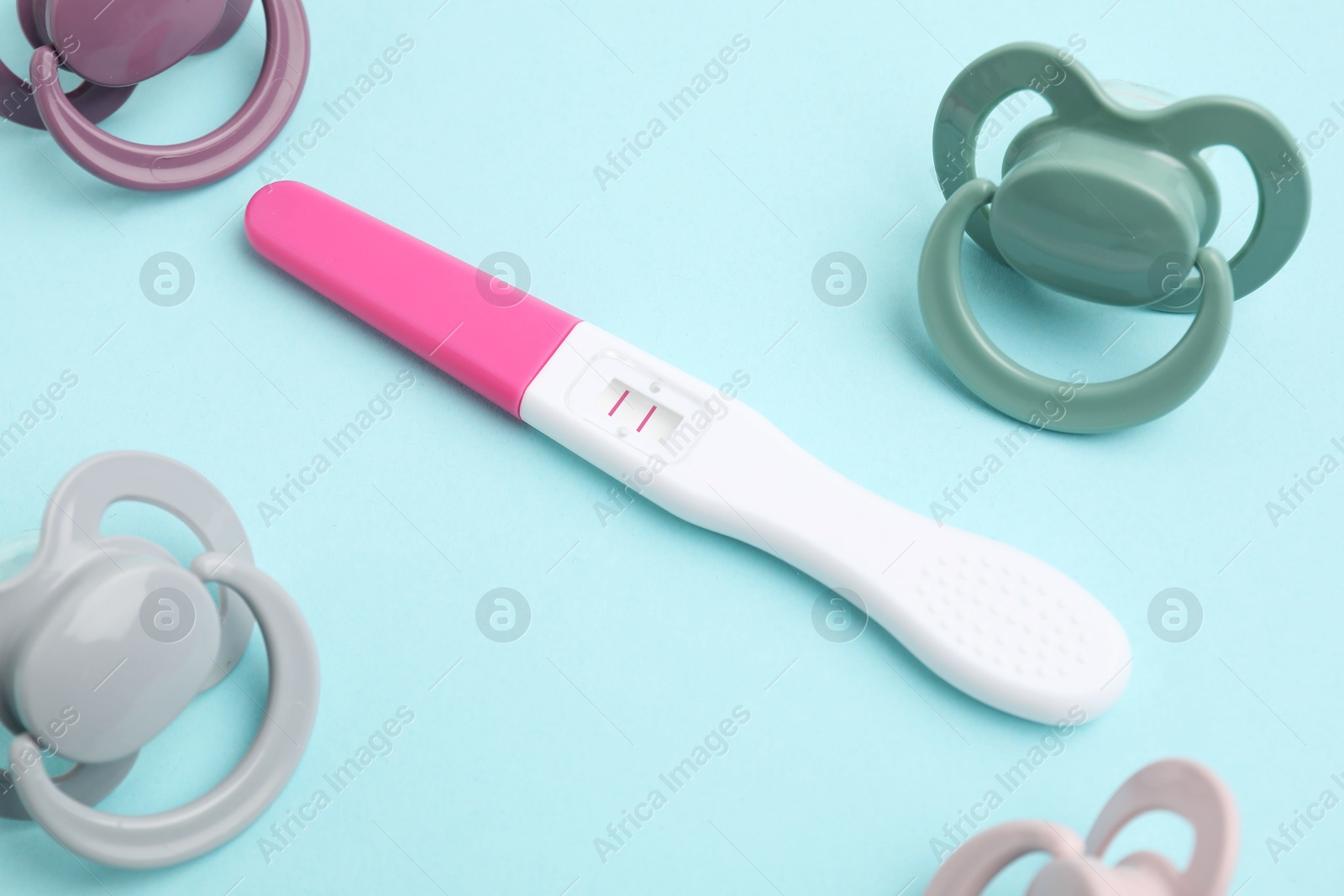 Photo of Pregnancy test and pacifiers on light blue background, closeup